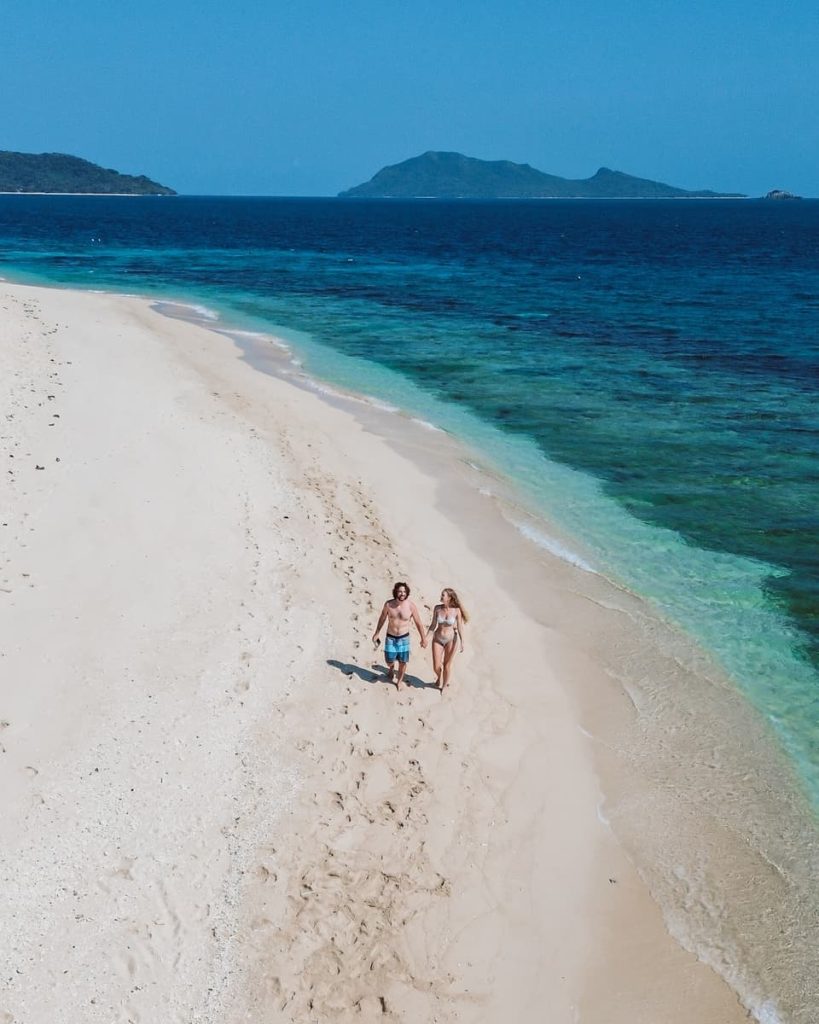 Couple walking along a quiet white sand beach in Coron, Palawan, during the dry season—one of the best times to enjoy the top things to do in Coron, Philippines.