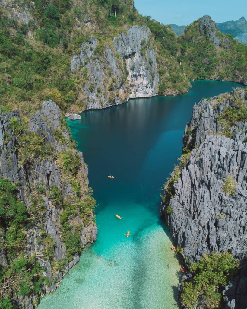 Aerial view of kayakers paddling through the crystal-clear entrance of Big Lagoon in El Nido, Philippines.