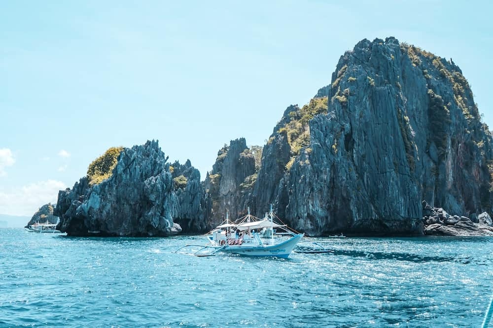 Traditional bangka boat cruising past towering limestone cliffs near Hidden Beach in El Nido