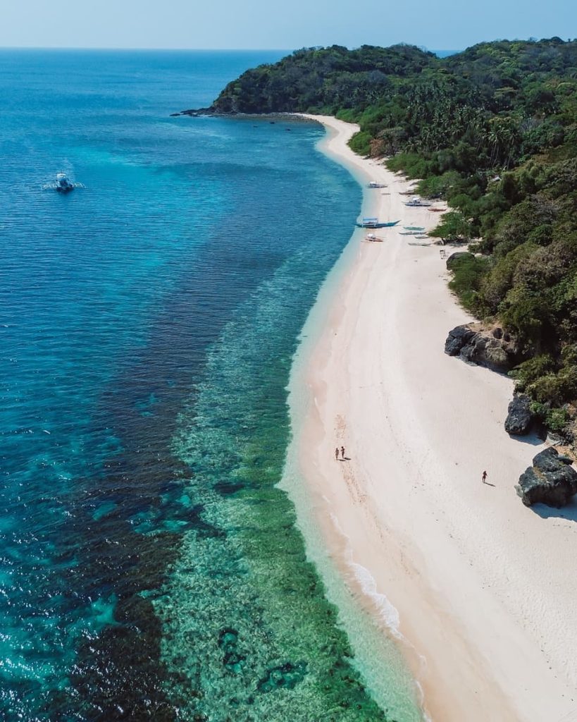 Aerial view of Nacpan Beach in El Nido with white sand and turquoise reef-lined shore—one of the best side-trip options from Coron, Philippines and a top thing to do in El Nido.