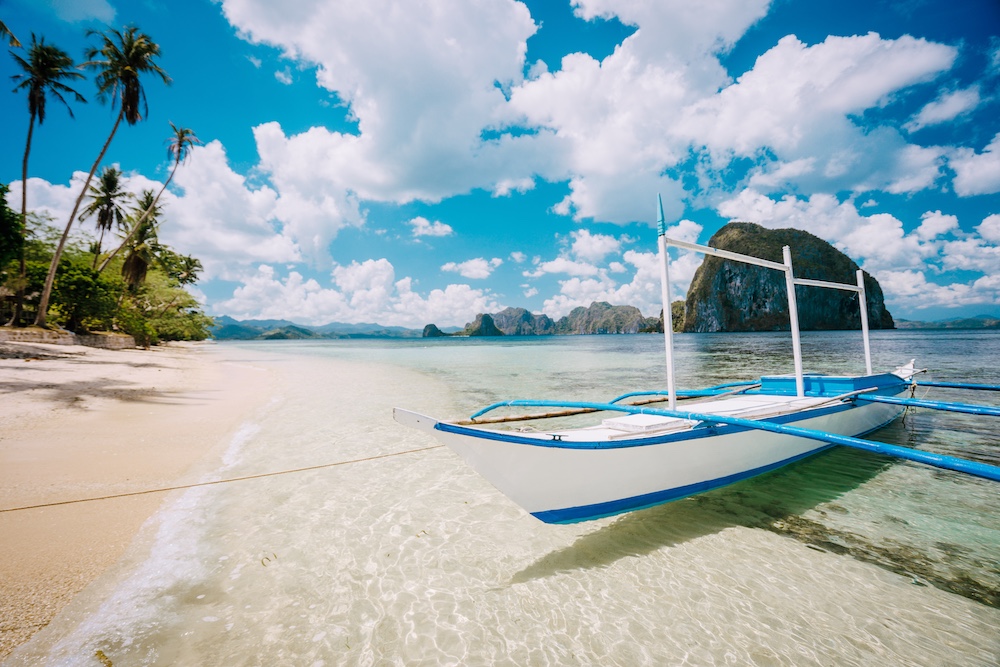 Traditional bangka boat on the crystal-clear shore of El Nido with dramatic limestone islands in the distance
