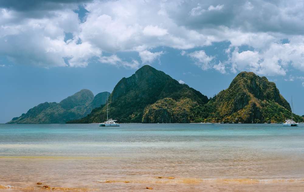 Peaceful view of yachts anchored off Corong-Corong Beach in El Nido with dramatic limestone islands in the distance—one of the most scenic and chill things to do near Coron, Philippines.
