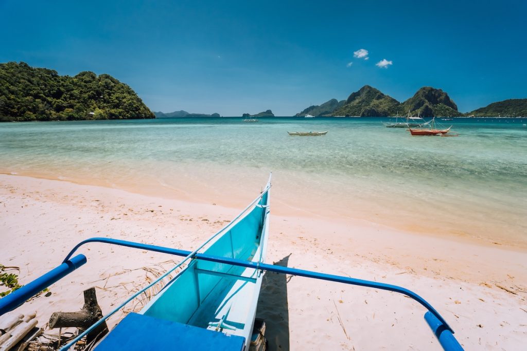Traditional banca boat at Las cabanas beach in front of blue lagoon and exotic nature scenery in El Nido, Palawan, Philippines.