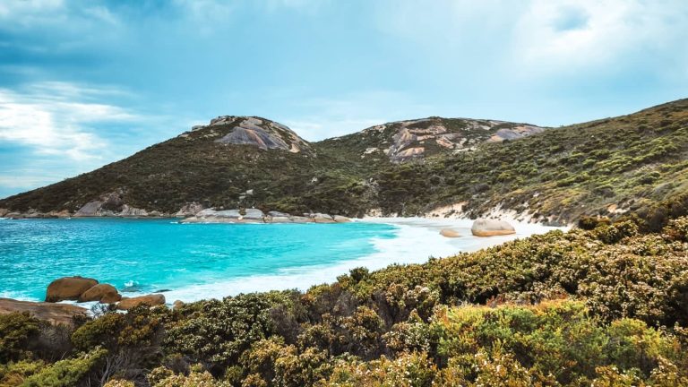 A vibrant turquoise bay framed by green hills and smooth granite boulders in South West Australia. This coastal scene captures the natural beauty found along a south west australia road trip 7 days itinerary.