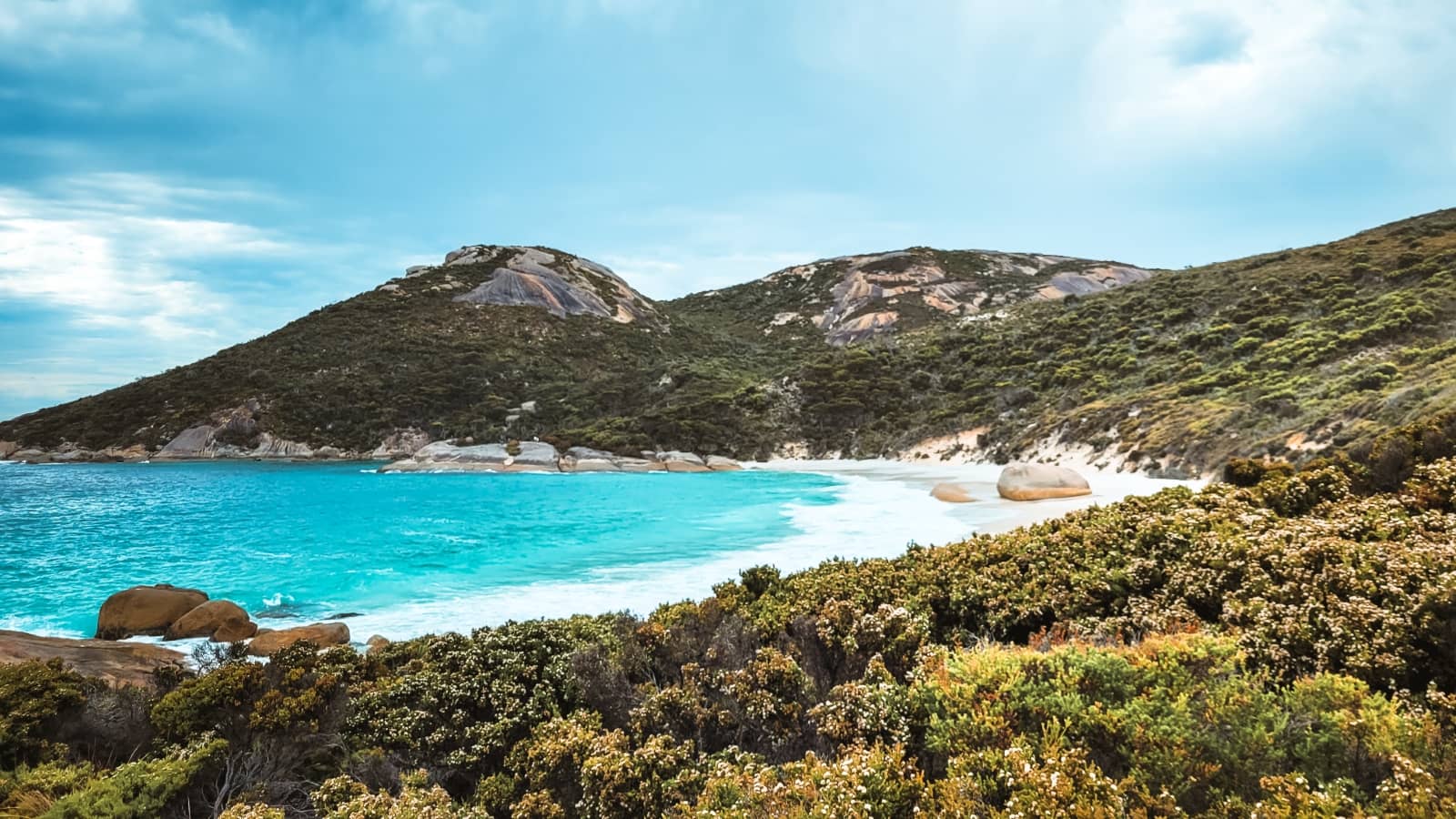 A vibrant turquoise bay framed by green hills and smooth granite boulders in South West Australia. This coastal scene captures the natural beauty found along a south west australia road trip 7 days itinerary.