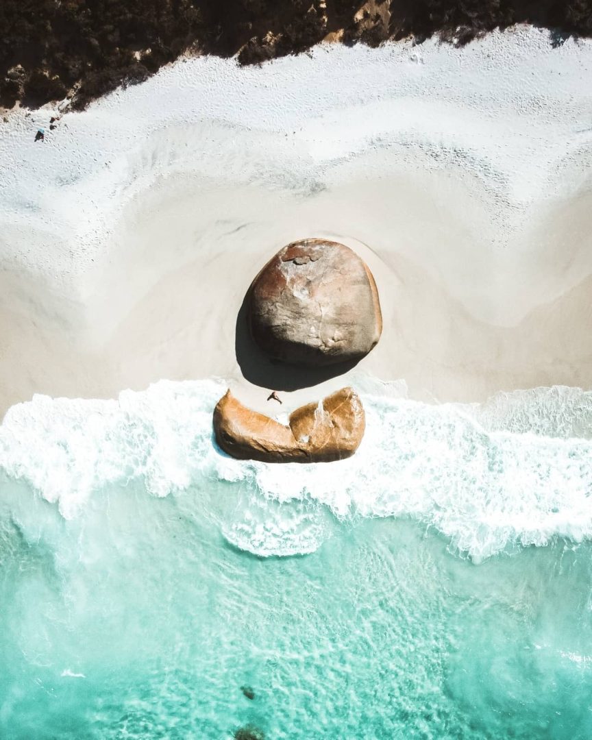 Aerial view of two large boulders on Misery Beach, Albany, WA, with turquoise waves crashing below. This dramatic coastline is a standout along a south west australia road trip 7 days.