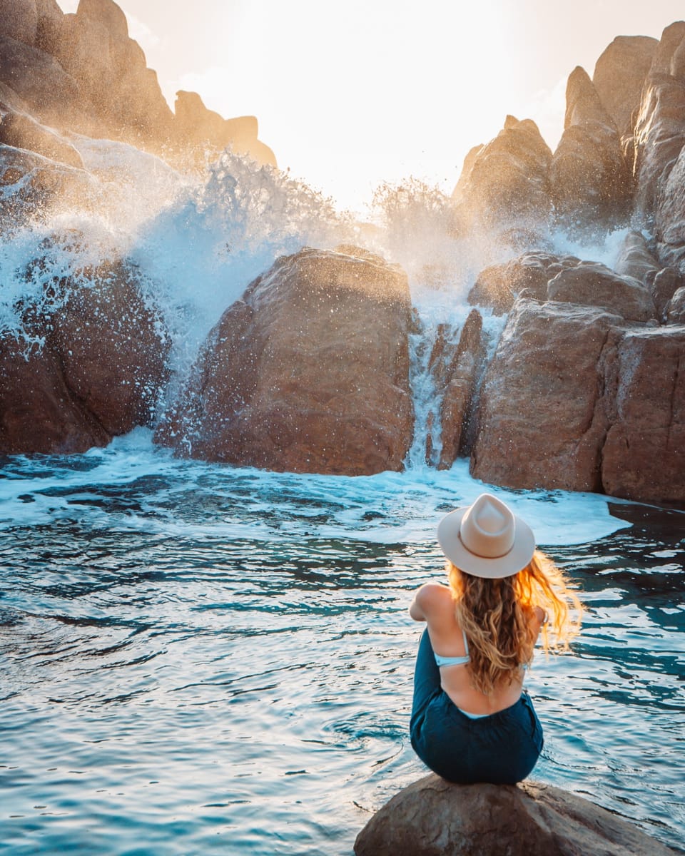 A woman sits on a rock watching waves crash at Injidup Natural Spa, Yallingup. This rugged coastline is a standout feature during a south west australia road trip 7 days.