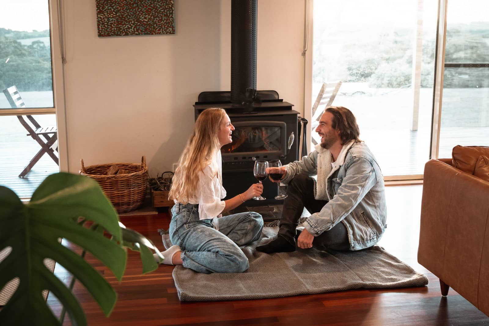 Couple sitting on a rug in front of a fireplace, toasting red wine during a cosy evening on a kangaroo island road trip 3 days.