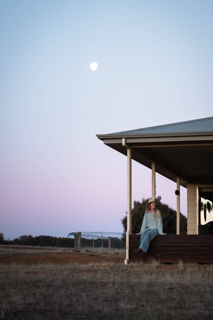 Woman sitting on a cabin deck under a pastel sky with the moon rising, soaking up dusk on a kangaroo island road trip 3 days.
