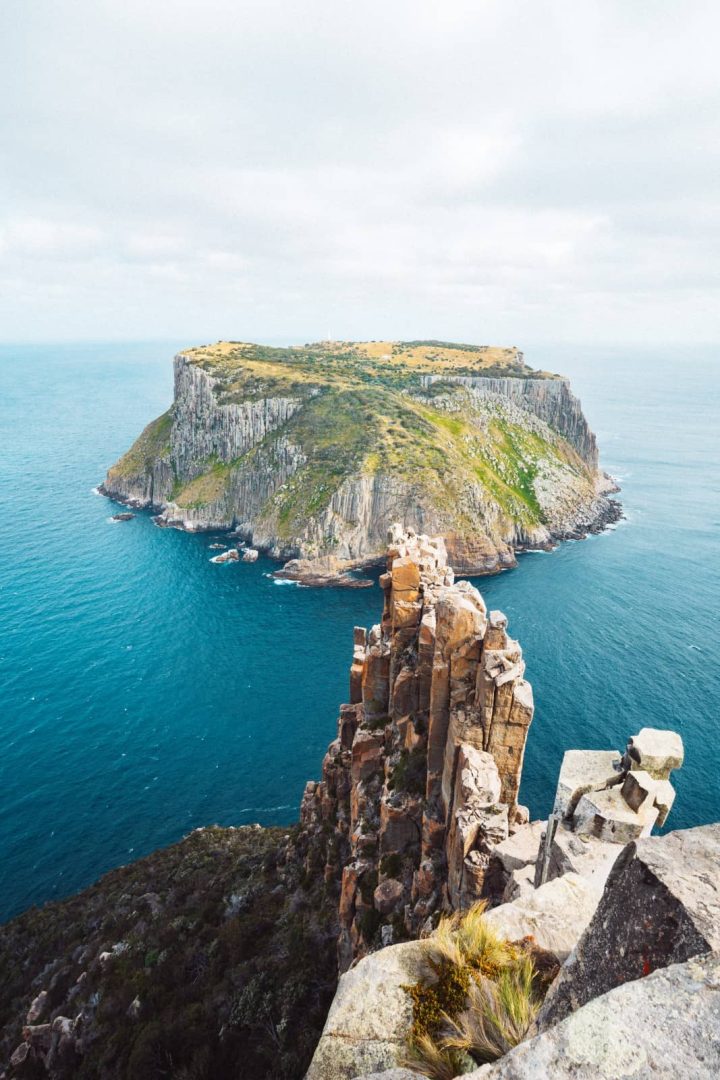 Tasman Island rising from the ocean, seen behind the dramatic dolerite spires of Cape Pillar, one of the most iconic views on the Three Capes Track for free.