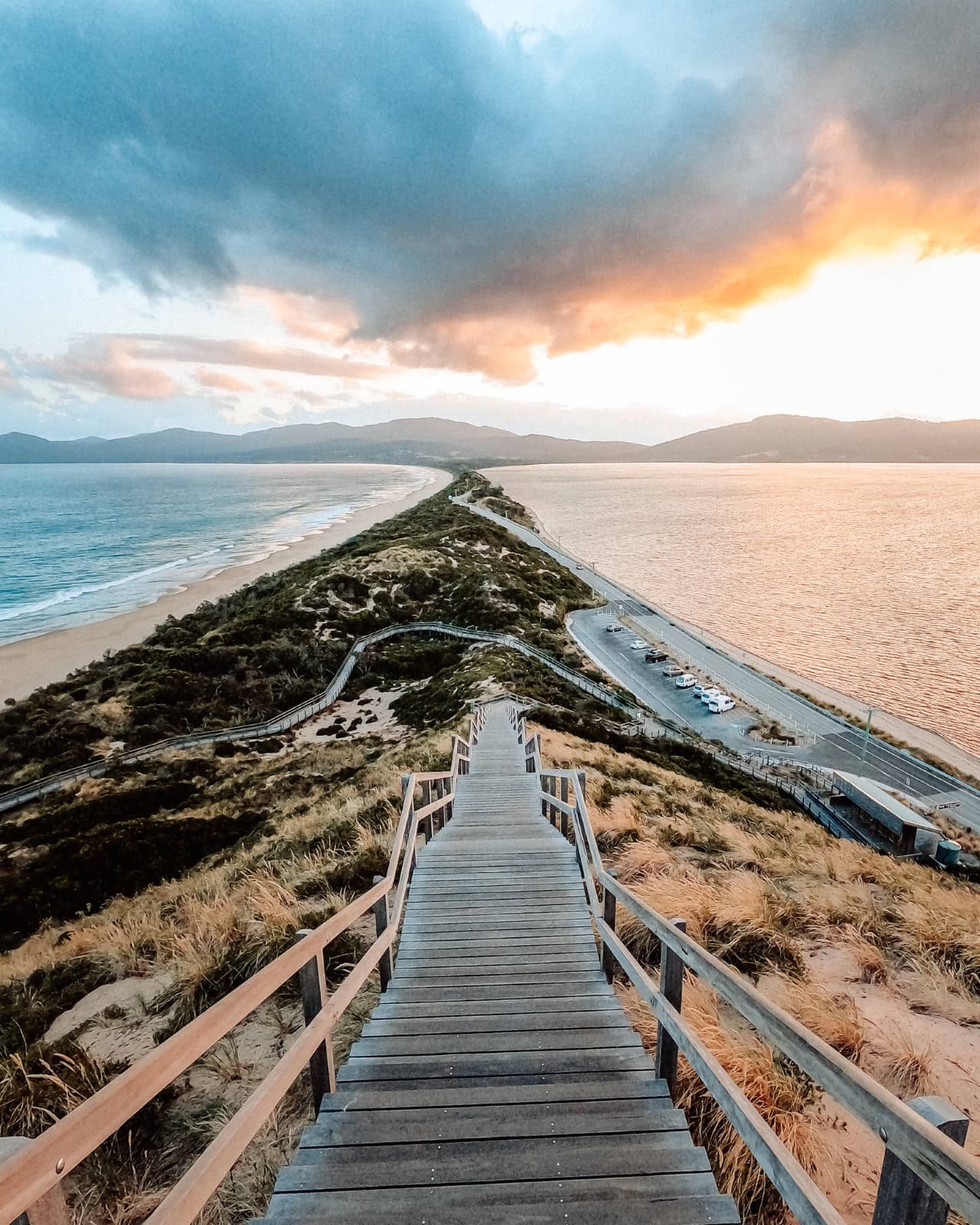 Wooden staircase of Truganini Lookout leading down to The Neck on Bruny Island at sunset, with narrow land connecting two parts of the island between the ocean and bay, one of the most iconic things to do in Tasmania.