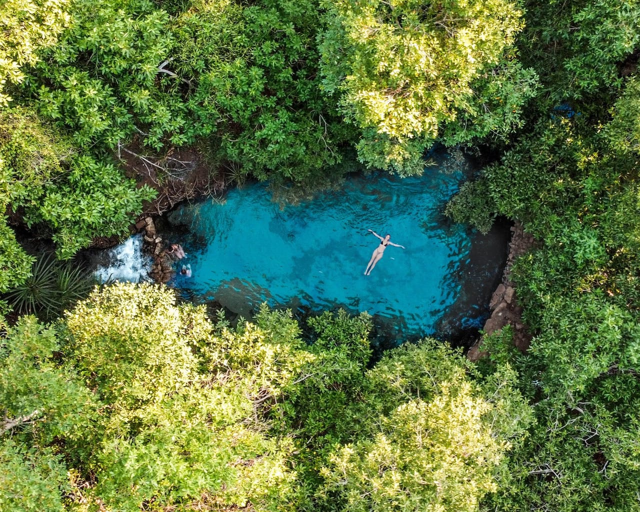 Aerial view of a person floating in the bright turquoise waters of the secluded Katherine Hot Springs, encircled by lush greenery, a tropical highlight of a road trip to Katherine.
