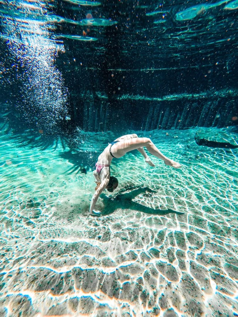 A woman bends backwards underwater in the exceptionally clear water at Mataranka Hot Springs. Sunlight creates rippling patterns across the sandy bottom and shows just how clear the thermal pool is.