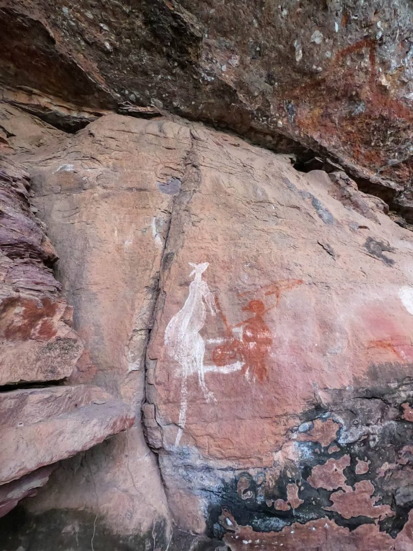 White and red Aboriginal rock art depicting a kangaroo and other figures on a weathered sandstone wall at Burrungkuy Nourlangie Rock. The culturally significant site is a memorable stop on a Darwin to Kakadu weekend road trip.