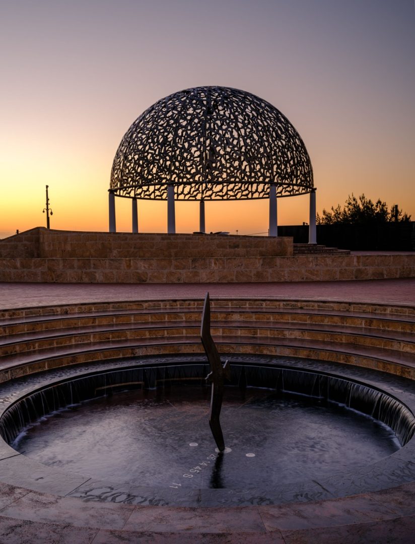 HMAS Sydney II Memorial in Geraldton at sunset with the silver dome silhouetted against an orange sky and the circular Pool of Remembrance in the foreground. Source. Tourism Western Australia.