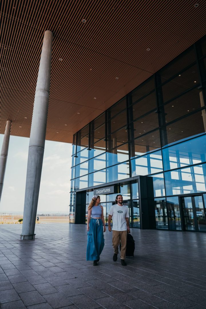 A couple walking out of the terminal at Western Sydney International Airport with their luggage, under the timber-slatted canopy.