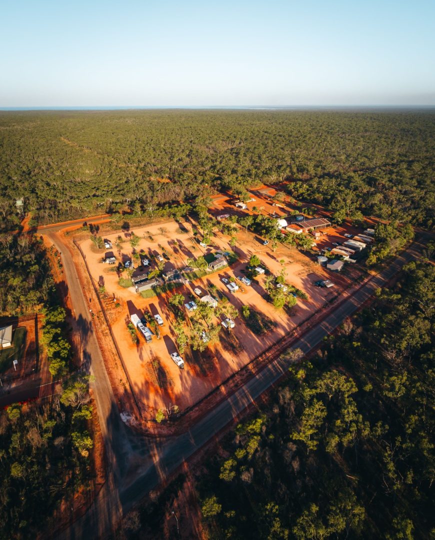 Aerial view of Djarindjin Campground, Dampier Peninsula, Western Australia, surrounded by dense green bushland. Caravans and campsites sit among trees and red dirt roads.
