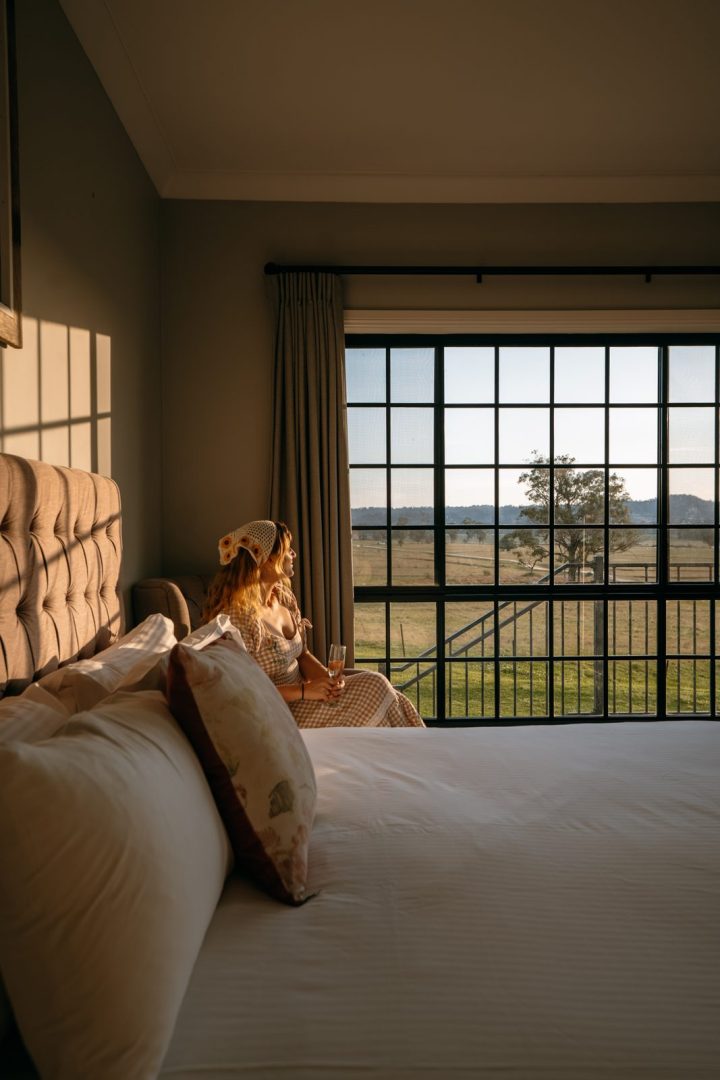 A woman relaxing on the bed beside a big window overlooking the countryside in a room at Camden Valley Inn.